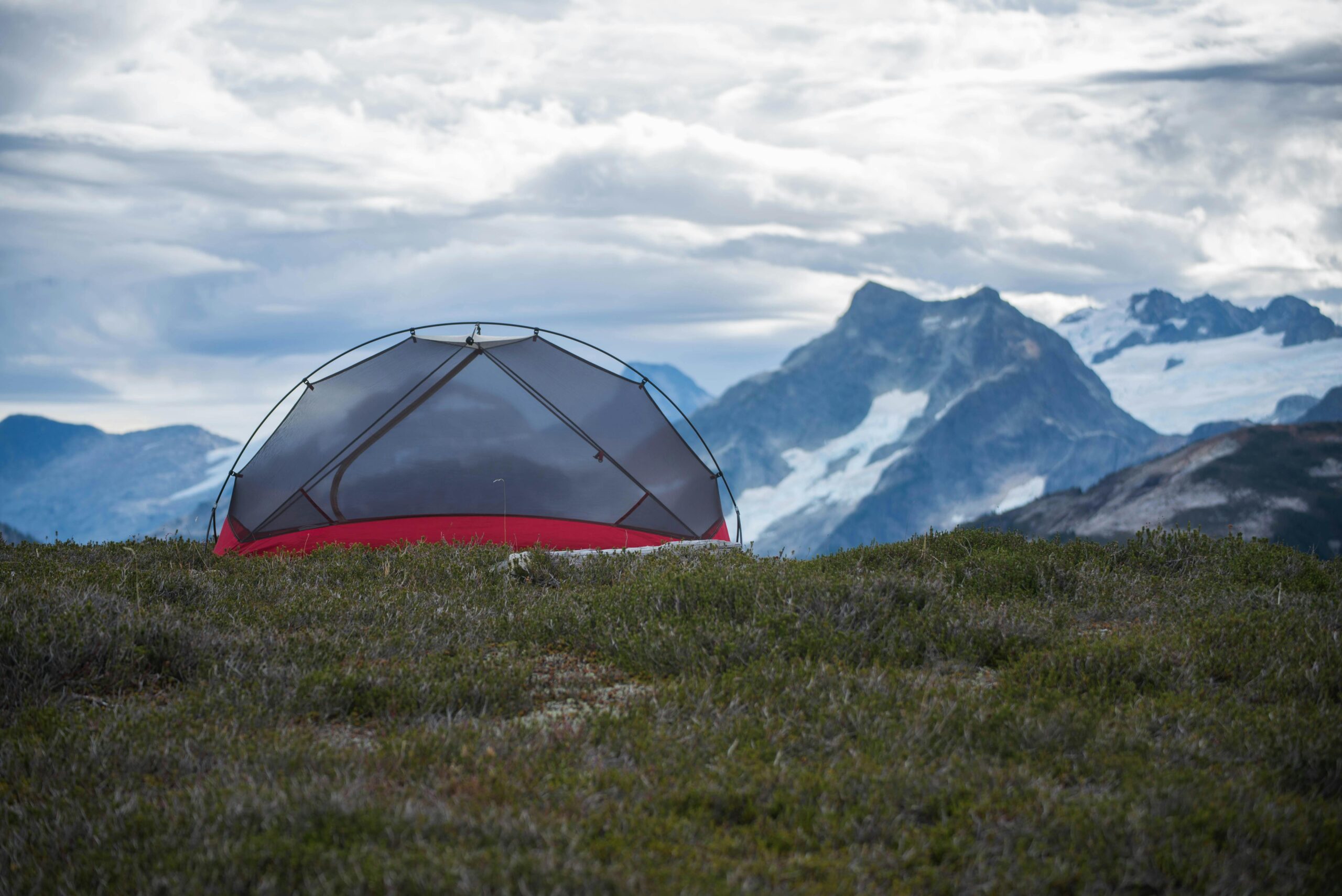 A lone tent set against a majestic mountain backdrop under cloudy skies.